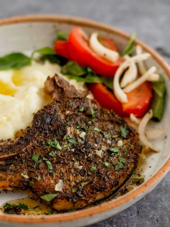 Pan Seared Pork Chop in a plate with mashed potatoes and tomato onion lettuce salad