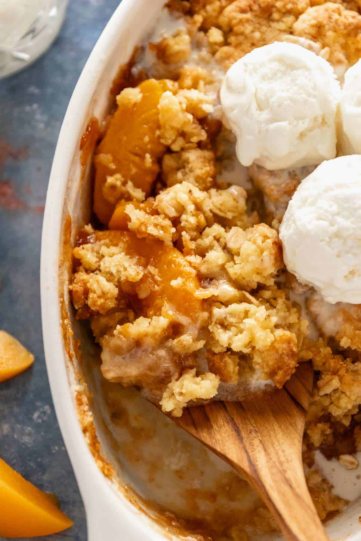 peach cobbler in oval baking dish with ice cream.