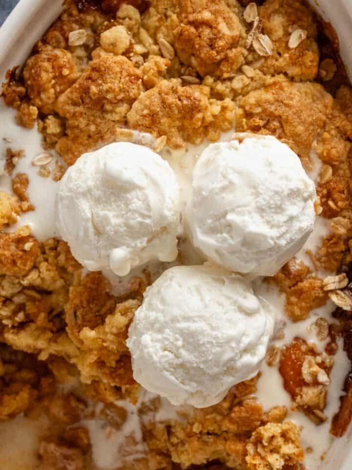 peach cobbler in oval baking dish with ice cream.