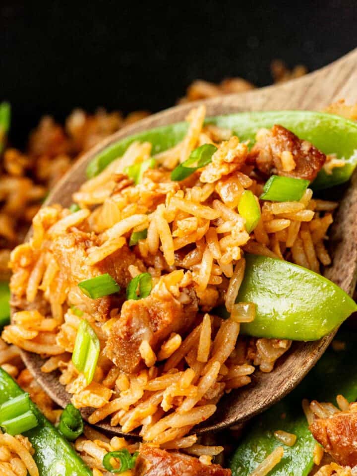 bbq pork fried rice in a wok skillet and a wooden spoon taking out the rice