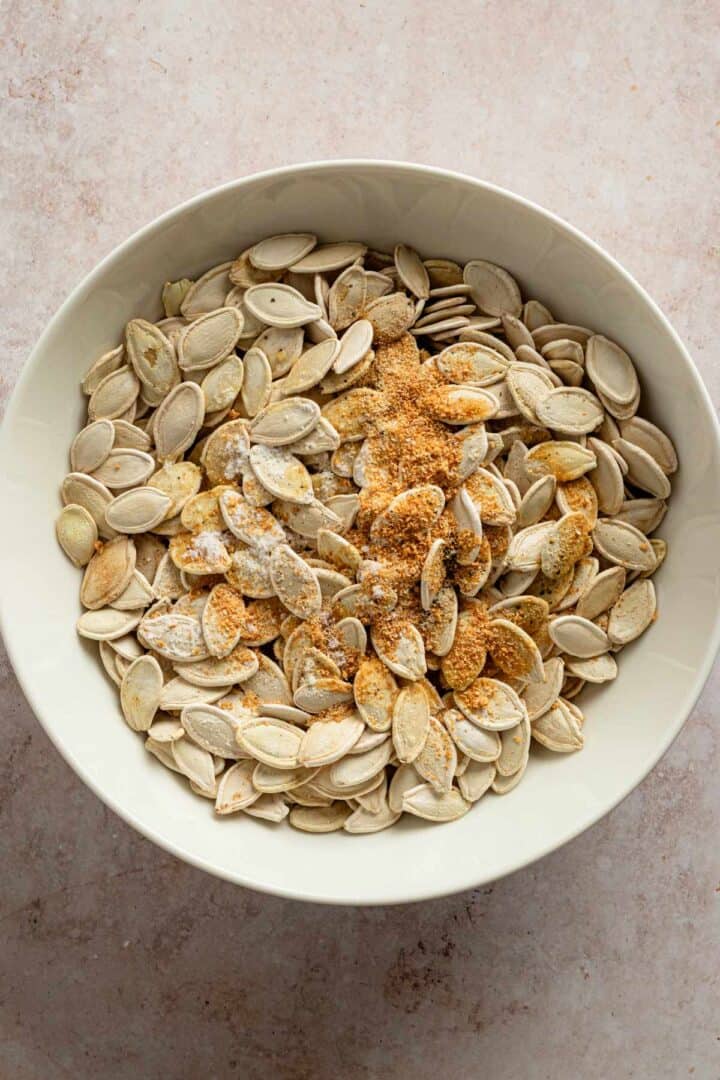 raw pumpkin seeds with seasonings in a bowl.