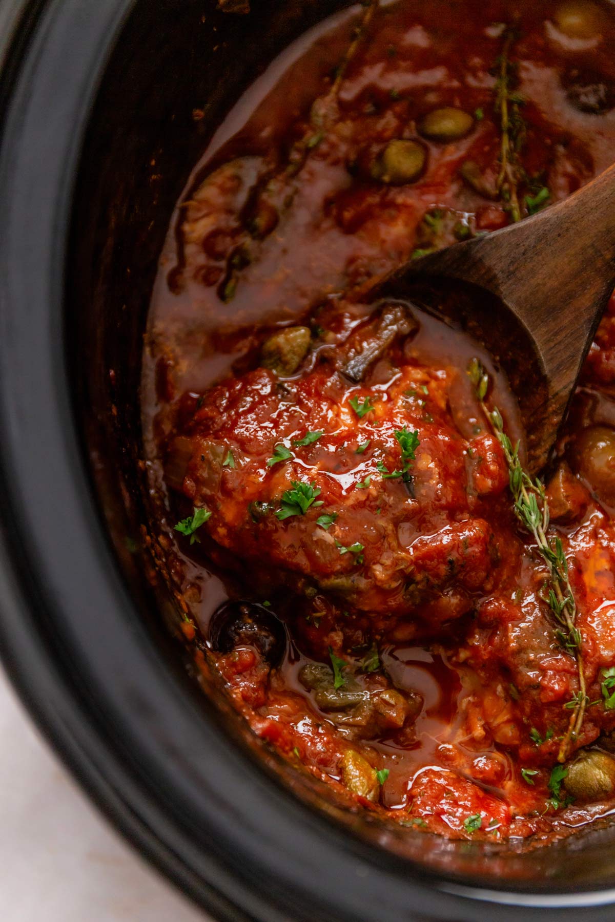 a close up shot of slwo cooker chicken thighs in tomato sauce and Italian seasonings and olives (Chicken Cacciatore)