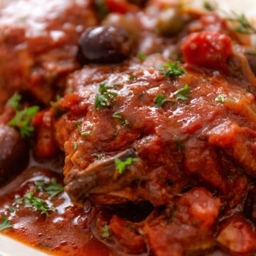 a close up shot of slow cooker chicken thighs in tomato sauce and Italian seasonings and olives (Chicken Cacciatore)