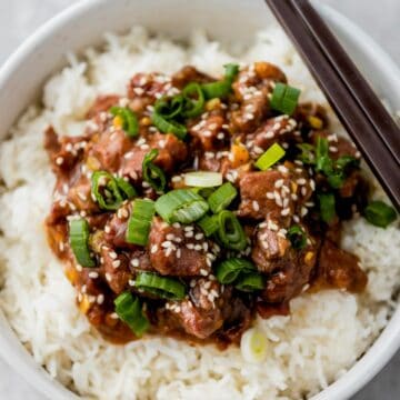 slow cooker mongolian beef over bed of rice and garnished with scallions