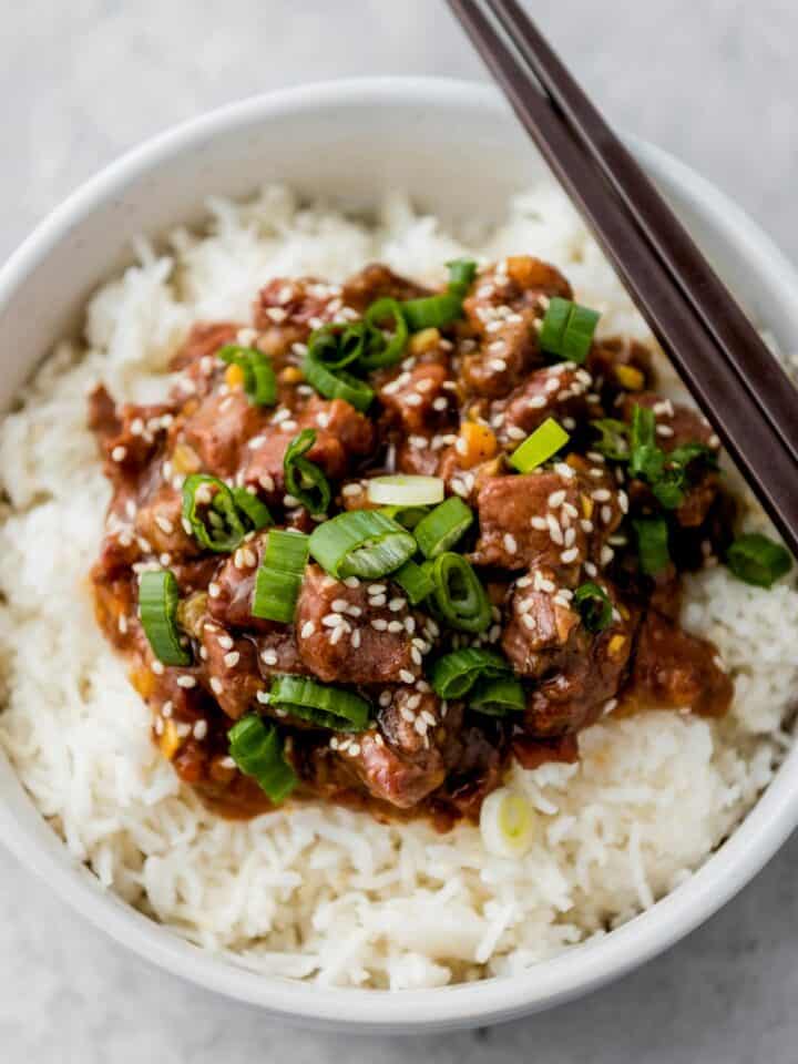 slow cooker mongolian beef over bed of rice and garnished with scallions