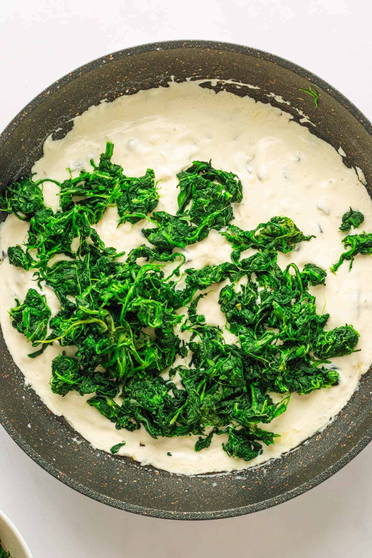 Spinach and creamy sauce in skillet.