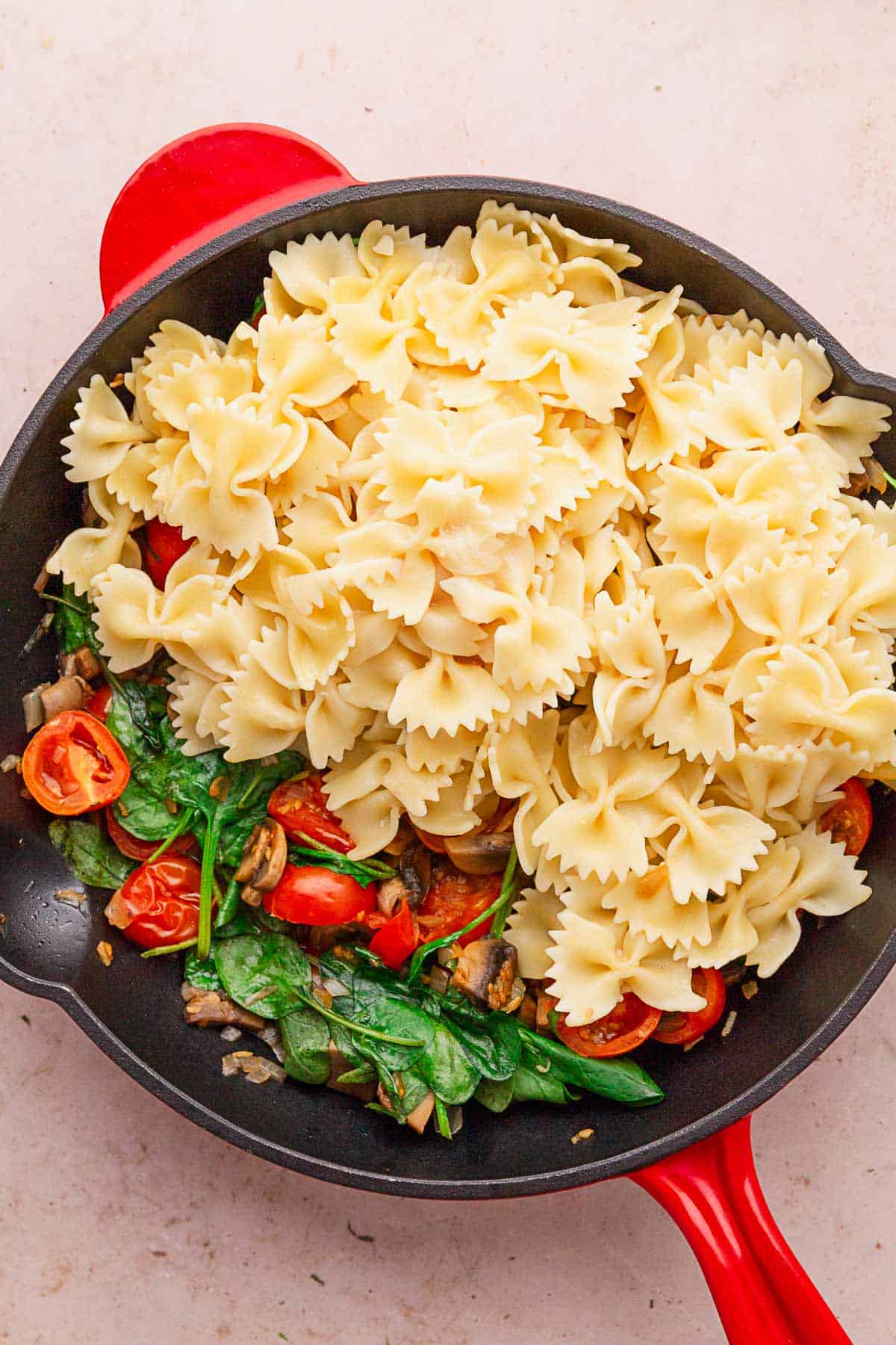 adding cooked and drained pasta back to the skillet with vegetables.