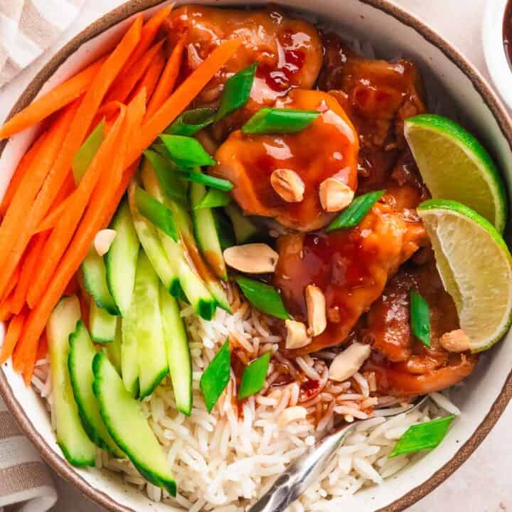 Thai chicken bowl with rice, carrots, and cucumber slices.