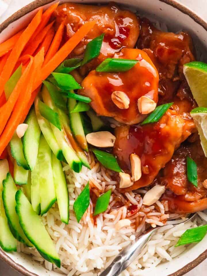 Thai chicken bowl with rice, carrots, and cucumber slices.