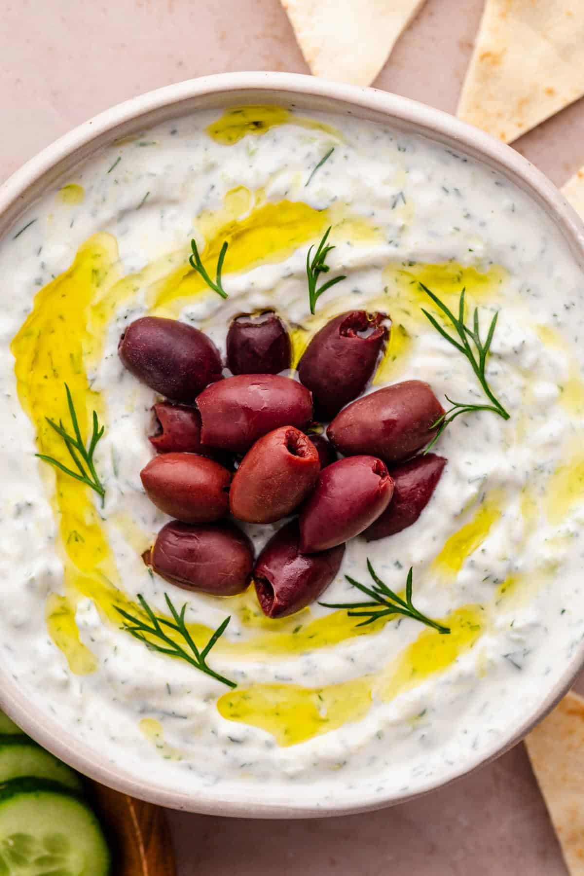 tzatziki sauce in a bowl with kalamata olives and drizzled with olive oil on top.