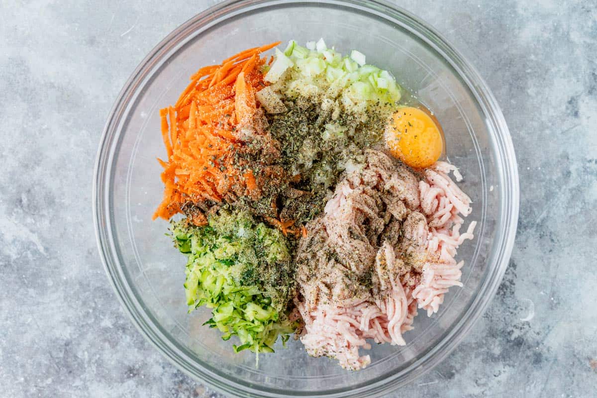 grated zucchini ground chicken carrots and egg in a glass bowl